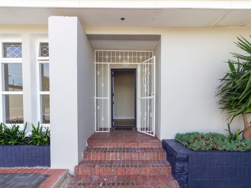 Front entrance of the office building featuring brick steps, a white security gate, and built-in planters with established greenery.