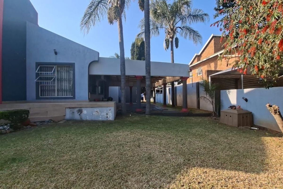 Rear view of the property featuring a covered patio area, concrete columns, and a spacious lawn with boundary walling.