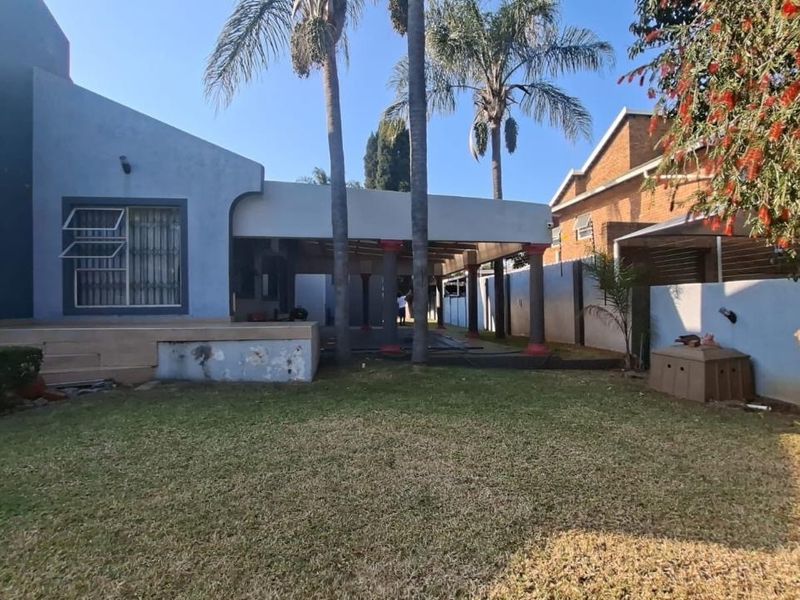 Rear view of the property featuring a covered patio area, concrete columns, and a spacious lawn with boundary walling.