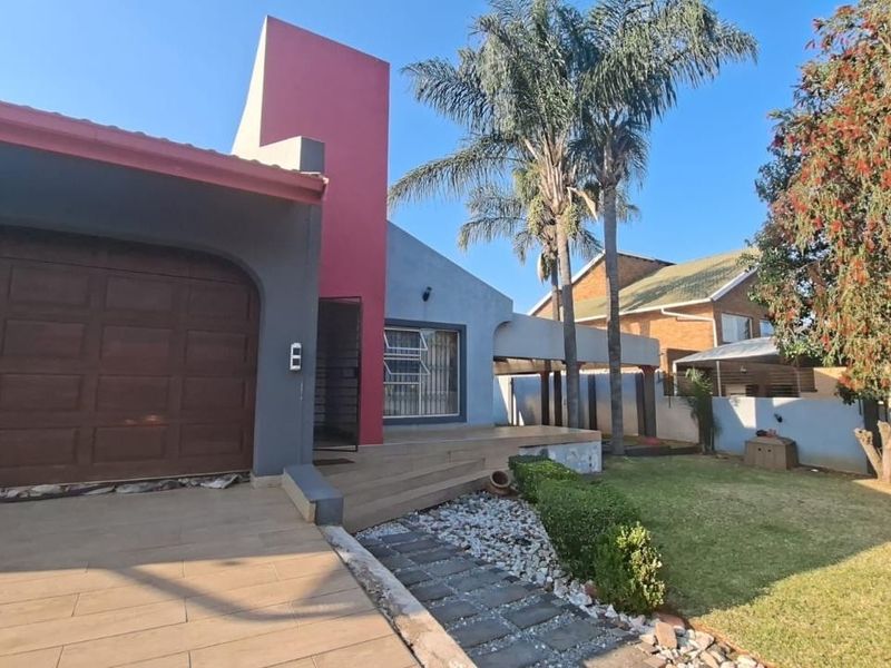 Front view of the property featuring a garage, tiled driveway, landscaped garden, and paved walkway leading to the entrance.