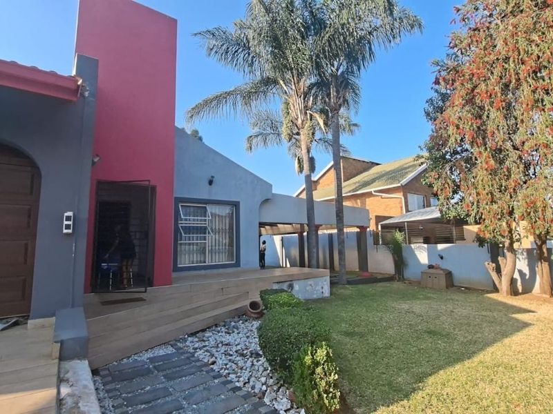 Front exterior view of the house featuring a tiled patio, stone pathway, landscaped garden, and secure garage access.