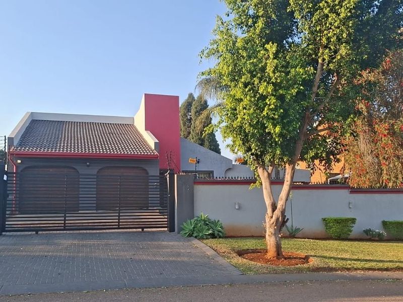 Front view of the property featuring a paved driveway, double garage with automated doors, and a secure perimeter wall with electric fencing.