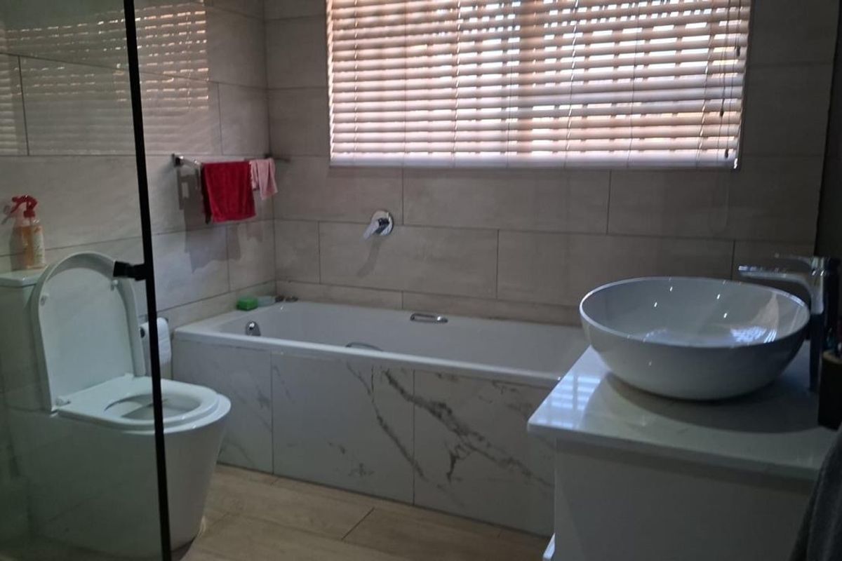 Modern bathroom featuring a built-in bathtub, vessel sink on a vanity cabinet, wall-mounted toilet, and glass shower screen with neutral wall tiling.
