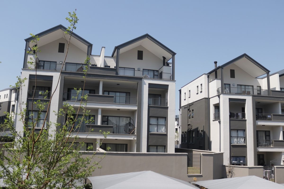 A view of the rear elevation of a modern apartment complex featuring multi-level balconies, contemporary architectural design, and a secure perimeter wall.