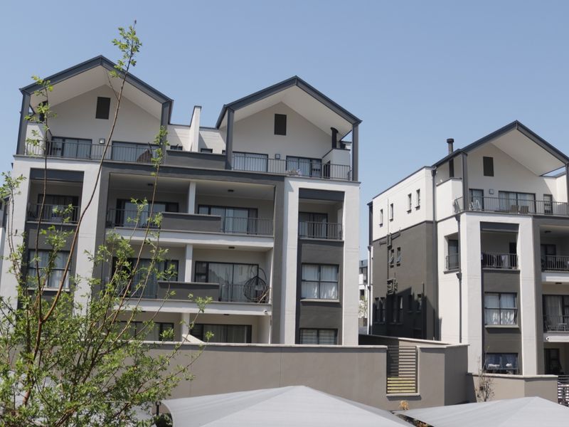 A view of the rear elevation of a modern apartment complex featuring multi-level balconies, contemporary architectural design, and a secure perimeter wall.