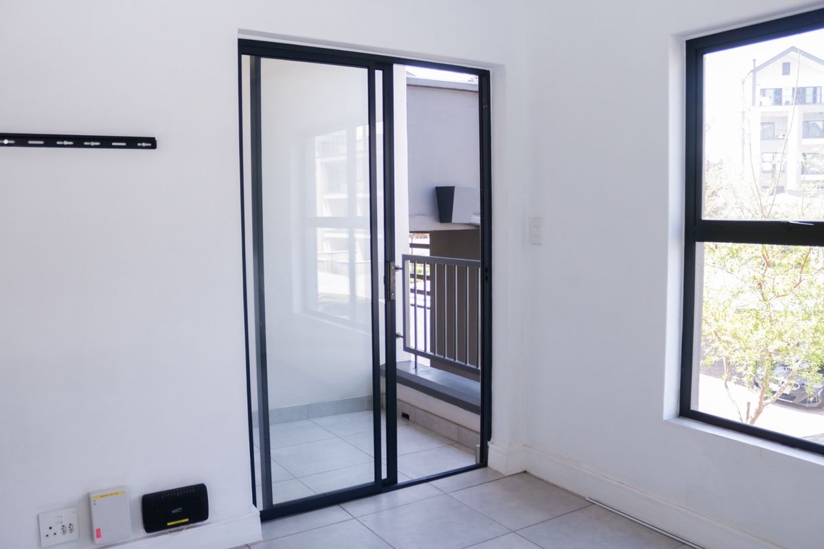 Bright living area featuring neutral tiled flooring, modern black aluminum sliding doors leading to a balcony, and large windows providing natural light.