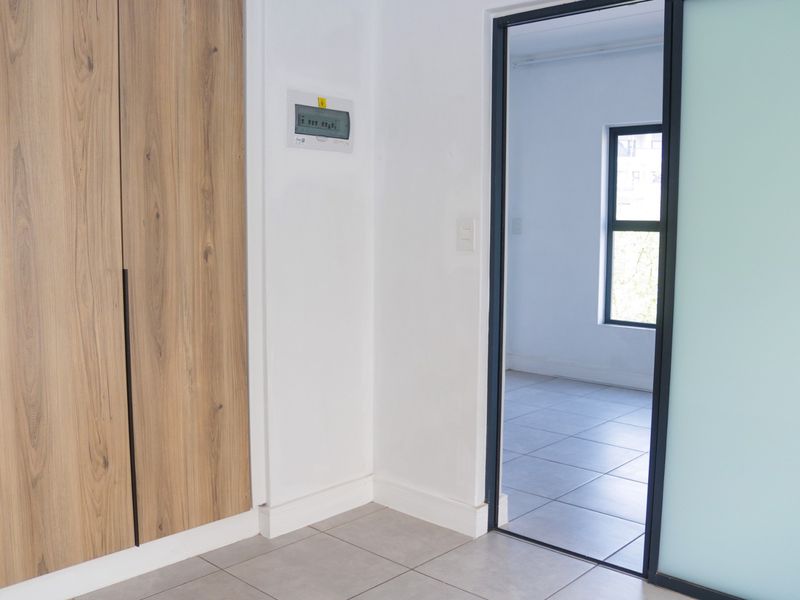 A clean, modern hallway featuring wood-finish built-in cupboards, tiled flooring, and a sliding door leading into an adjacent room.