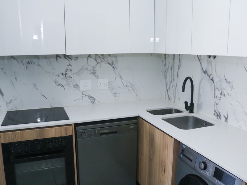 Modern kitchen featuring white quartz countertops, marble-look splashback, integrated appliances, and sleek cabinetry with a contemporary black mixer tap.