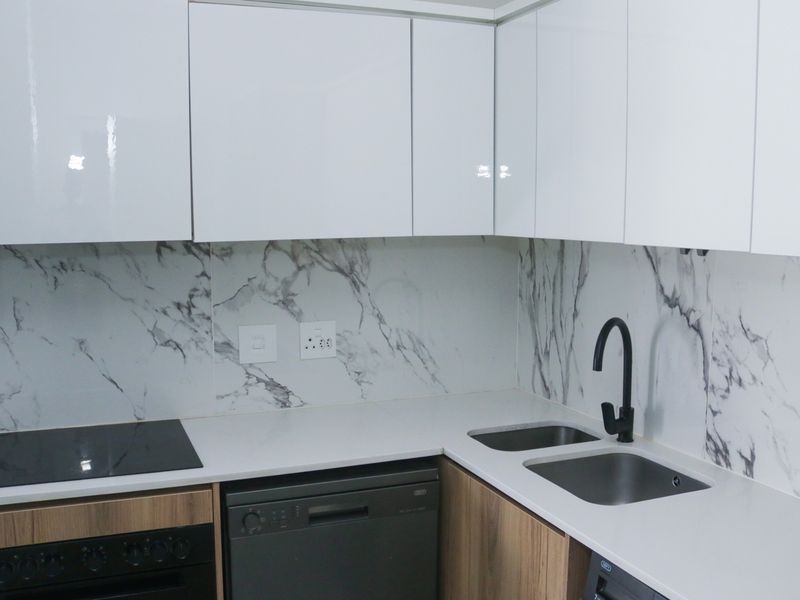 Modern kitchen featuring sleek white cabinetry, marble-look splashback, quartz countertops, integrated hob, oven, and a contemporary black mixer tap with double sink.