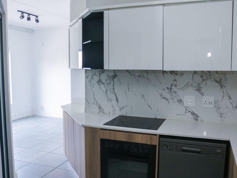 Modern kitchen featuring sleek white cabinetry, marble-effect splashback, built-in oven, electric hob, and integrated dishwasher, set against neutral tiled flooring.