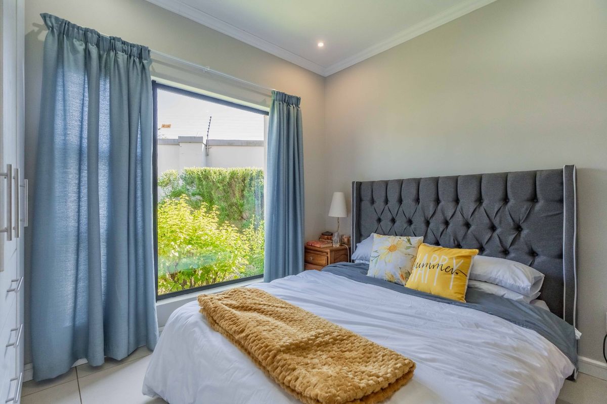 A well-maintained bedroom featuring built-in cupboards, elegant cornicing, recessed lighting, and a large window overlooking a private garden area.