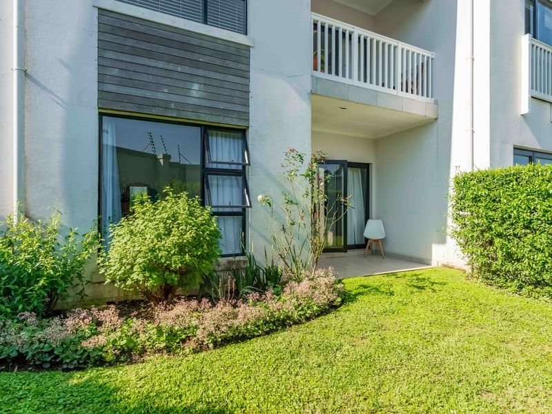 Rear view of the apartment featuring a private patio, landscaped garden, and an upper-level balcony with modern architectural finishes.