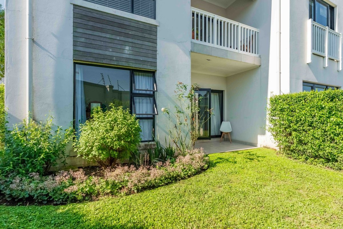 Rear view of the apartment featuring a private patio, landscaped garden, and an upper-level balcony with modern architectural finishes.
