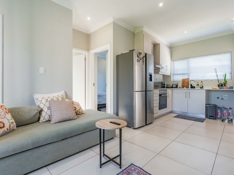 An open-plan living and kitchen area featuring tiled flooring, modern built-in cabinetry, integrated oven, and recessed lighting, creating a functional and cohesive living space.