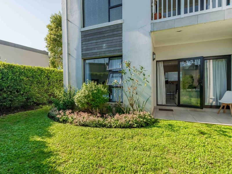 A ground floor apartment exterior featuring a private tiled patio, landscaped garden, and sliding glass door access to the interior living space.