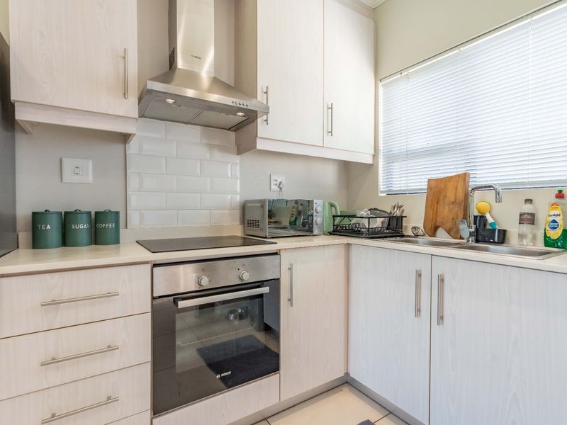 A well-maintained kitchen featuring light wood-grain cabinetry, subway tile backsplash, stainless steel appliances including an oven and extractor fan, and a functional sink area.