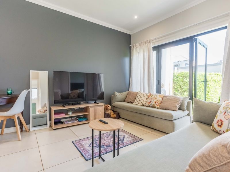A bright living room featuring large bi-fold glass doors that open to the outdoors, complemented by neutral tiled flooring and a modern grey feature wall.