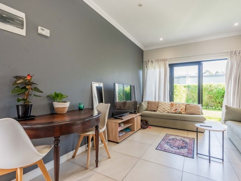 A bright living room featuring large format floor tiles, a dark accent wall, and a sliding glass door providing direct access to the garden.
