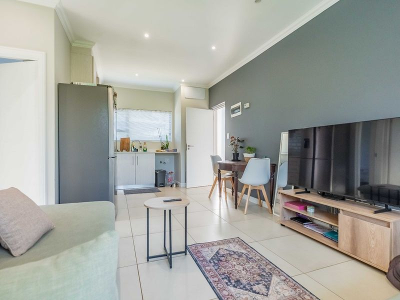 An open-plan living and kitchen area featuring neutral tiled flooring, recessed lighting, and a modern grey accent wall.