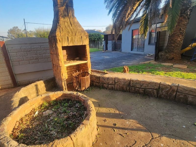 Rear garden area featuring a built-in brick braai, paved patio space, and raised stone planter, offering potential for an outdoor entertainment area.