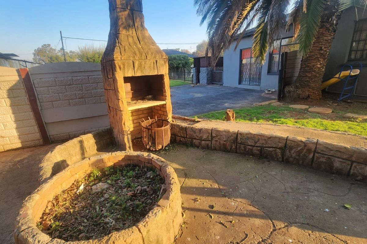 Rear garden area featuring a built-in brick braai, paved patio space, and raised stone planter, offering potential for an outdoor entertainment area.