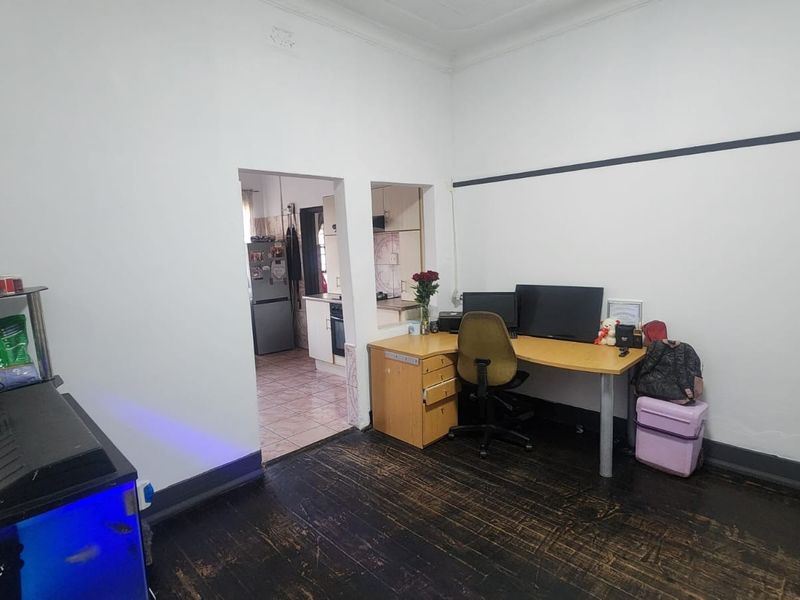 A functional office space featuring dark hardwood flooring, classic picture rails, and a coved ceiling, with a convenient pass-through opening to the kitchen area.