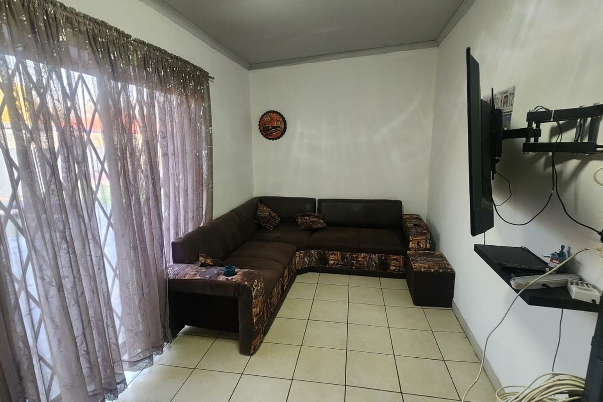 A functional living room featuring tiled flooring and a sliding glass door with security gate, providing access to the exterior.