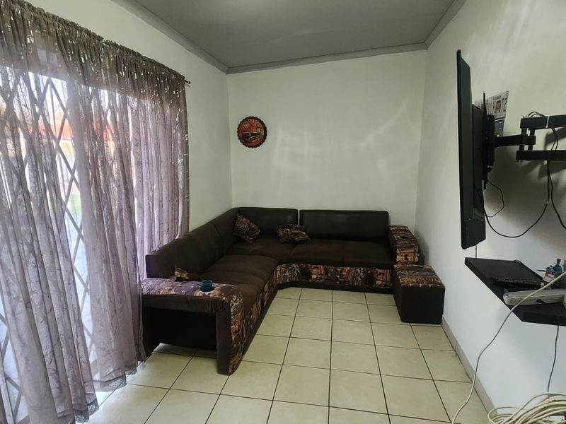 A functional living room featuring tiled flooring and a sliding glass door with security gate, providing access to the exterior.