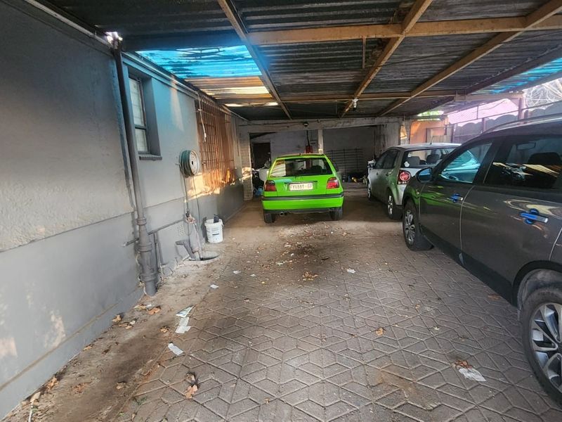 A covered carport or garage area featuring paved flooring and a corrugated metal roof structure.