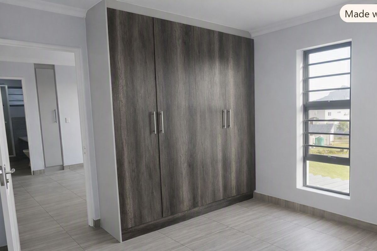 A bright, modern bedroom featuring neutral tiled flooring, built-in dark wood-grain cupboards, and a louvered window providing natural light.