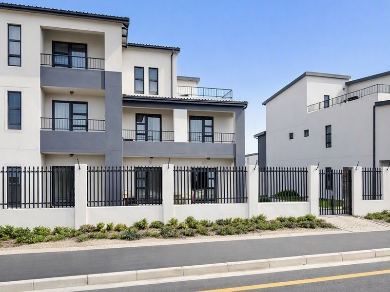 Modern apartment complex exterior featuring contemporary architecture, secure metal perimeter fencing, and private balconies with sliding glass doors.