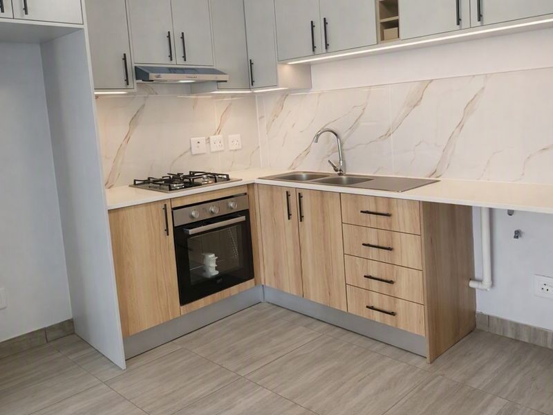 Modern kitchen featuring light wood cabinetry, marble-look splashback, gas hob, built-in oven, and integrated sink with contemporary finishes.