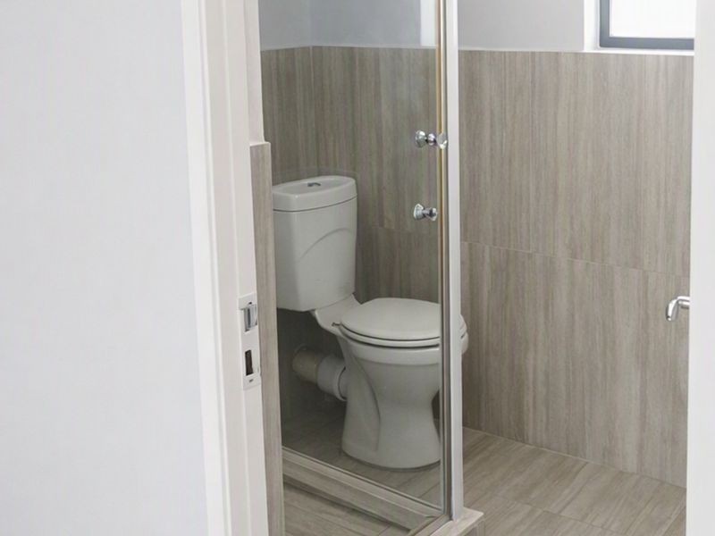 A clean, modern bathroom featuring a toilet and a glass-enclosed shower with neutral wood-look wall and floor tiling.