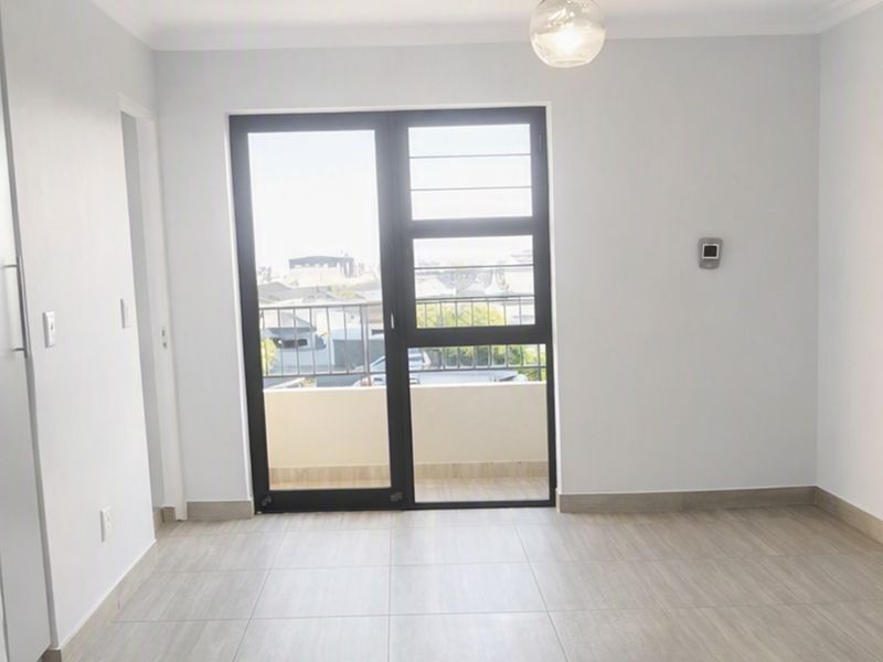 A bright, empty living area featuring modern tiled flooring, neutral walls, and a glass door leading to a private balcony.