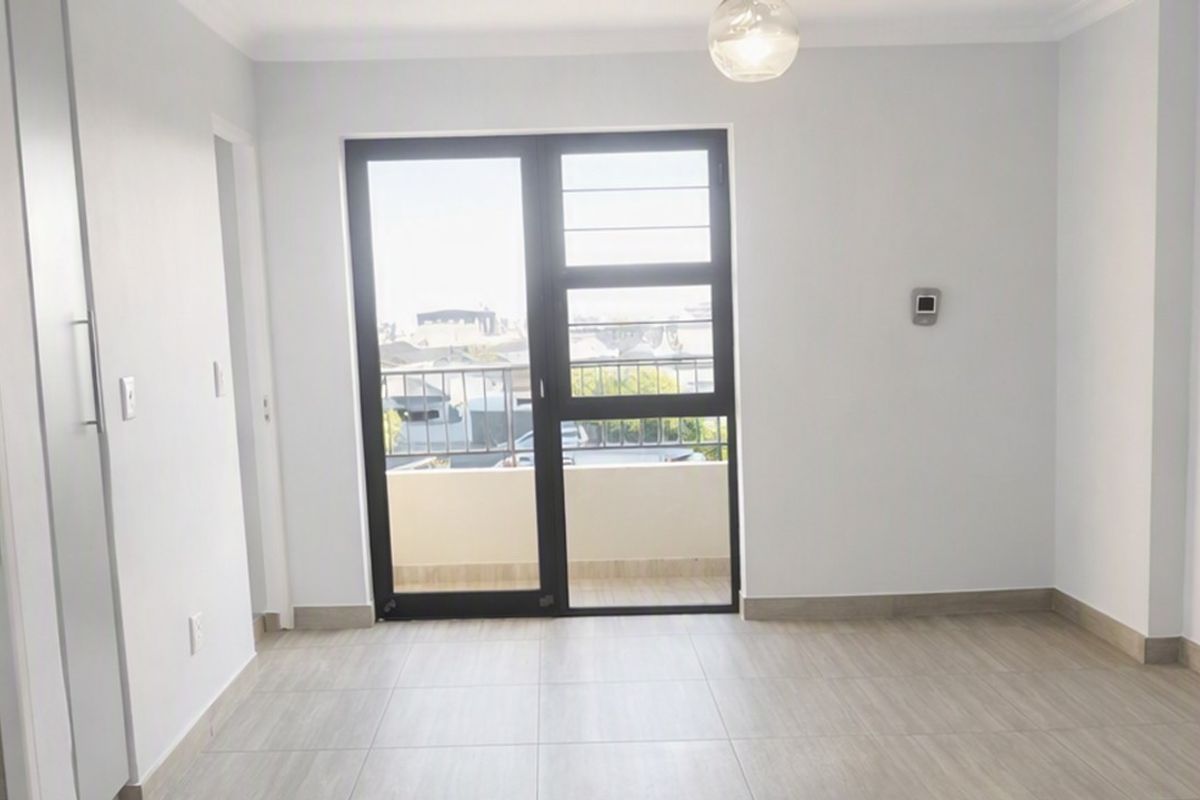A bright, empty living area featuring modern tiled flooring, neutral walls, and a glass door leading to a private balcony.