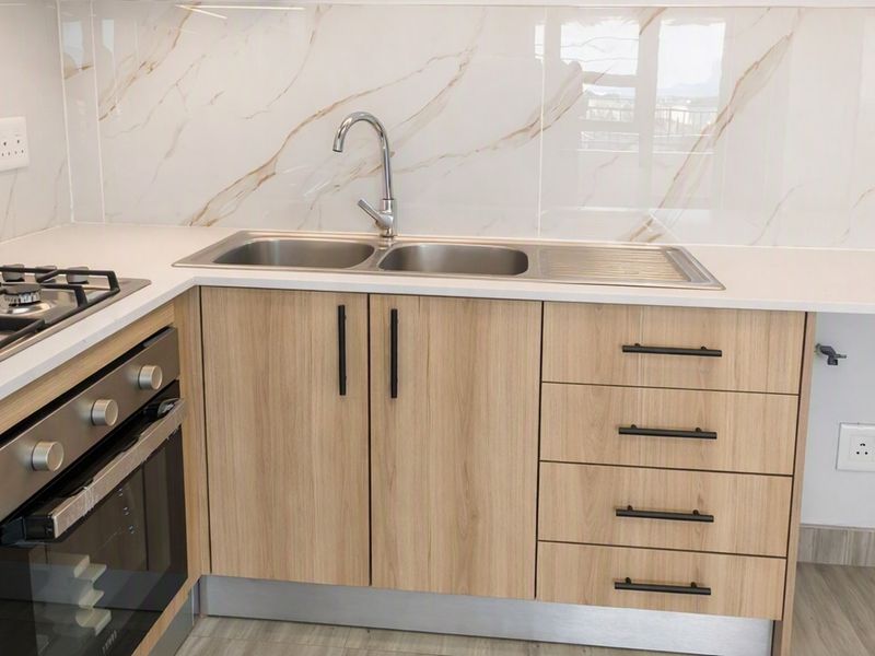 Modern kitchen featuring light wood cabinetry, quartz countertops, marble-look splashback tiles, a gas hob, and a built-in oven.