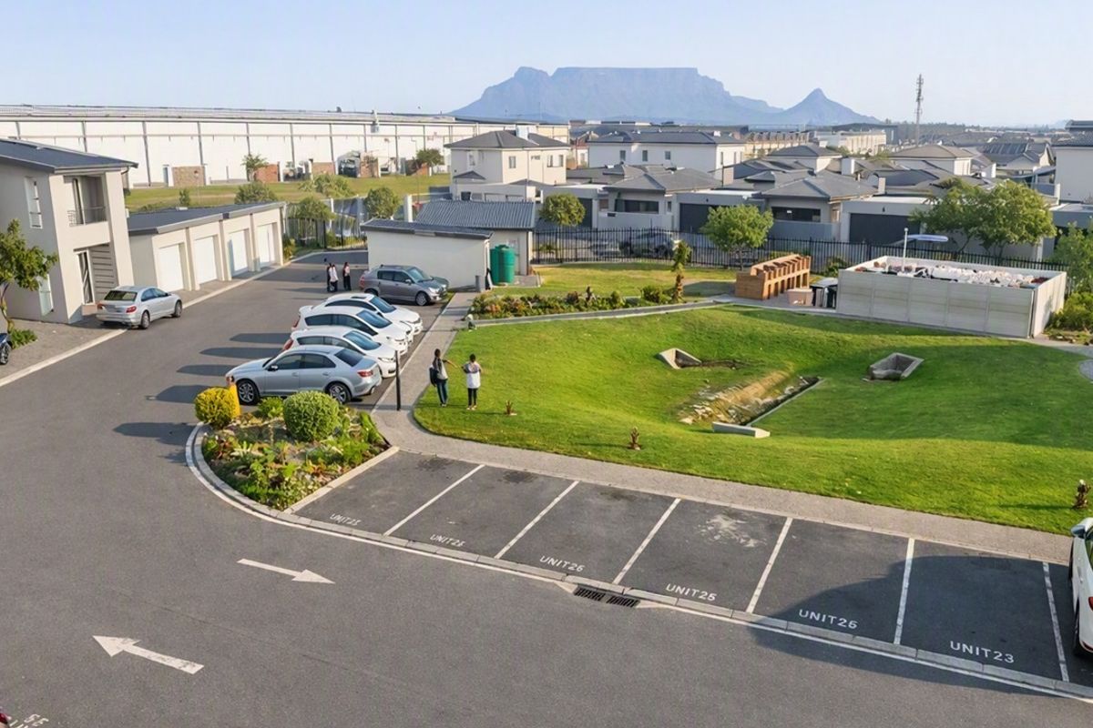 Aerial view of the apartment complex grounds featuring paved parking bays, landscaped green spaces, and views of Table Mountain in the distance.