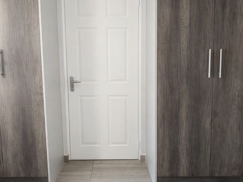 A clean bedroom interior featuring modern wood-grain built-in cupboards and neutral tiled flooring.