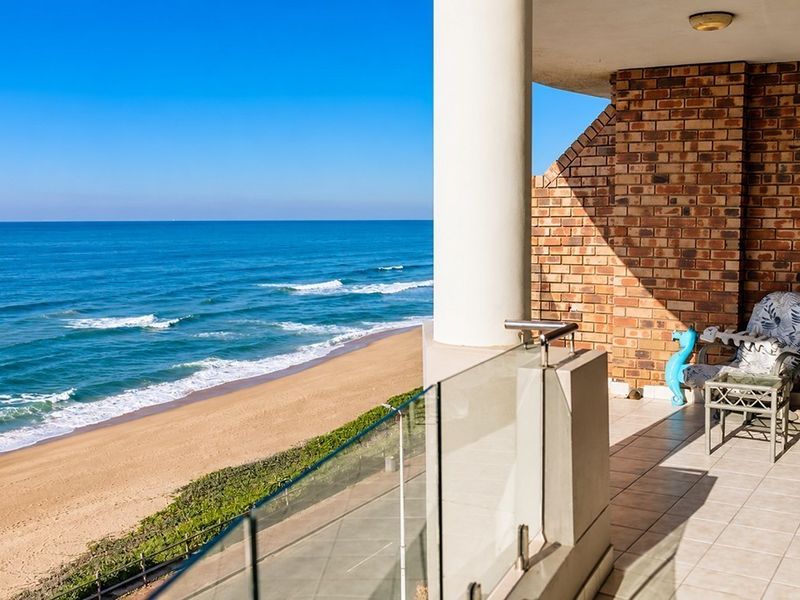 A spacious balcony featuring a glass balustrade and exposed brickwork, offering panoramic ocean and beach views.