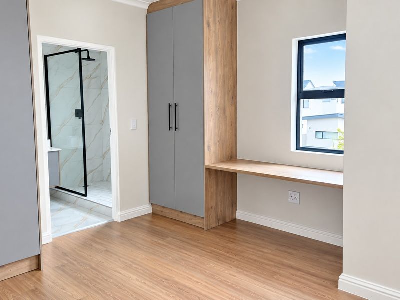 Modern bedroom featuring built-in cupboards, a integrated desk, laminate flooring, and direct access to an en-suite bathroom.