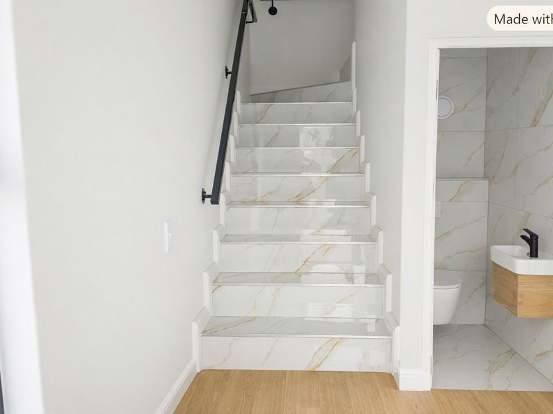A modern hallway featuring a tiled staircase with a black handrail, adjacent to a compact guest bathroom with a wall-mounted vanity and toilet.
