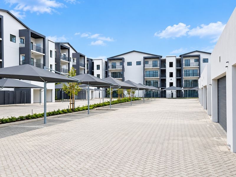 Modern townhouse complex featuring a paved parking area with shade cloth carports and multi-story residential units with balconies.