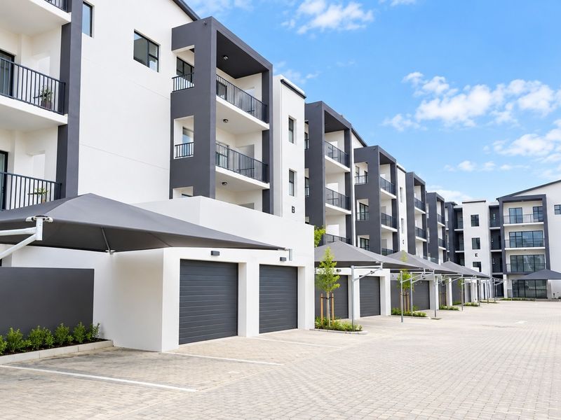 Modern townhouse complex exterior featuring a paved driveway, covered parking bays with shade sails, and multi-story residential units with private balconies.
