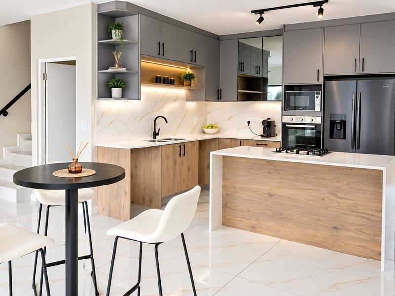 Modern open-plan kitchen featuring two-tone cabinetry, stone countertops, integrated appliances, and a central island, seamlessly flowing into the dining area and staircase.