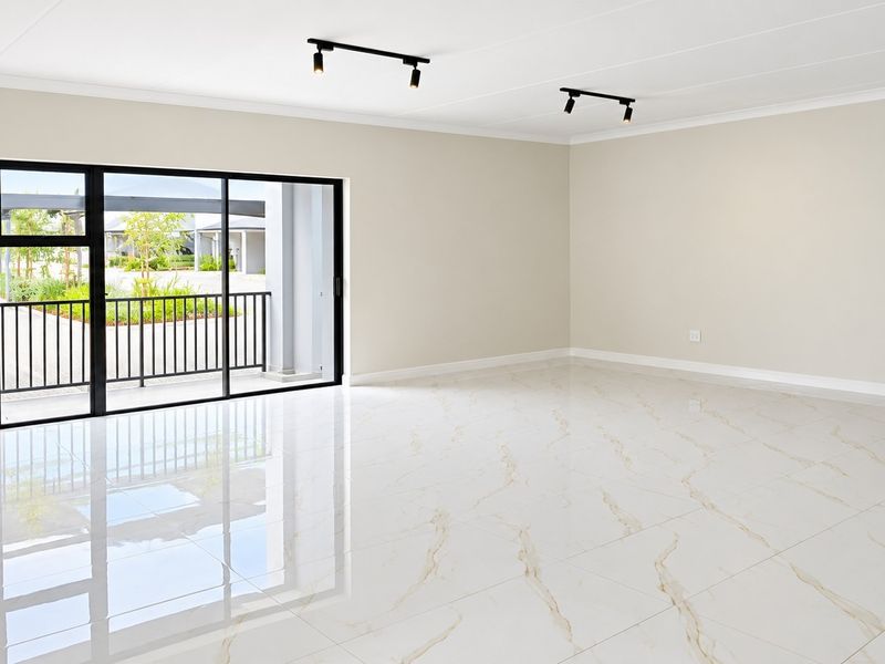 A bright, spacious, and empty living area featuring polished marble-look floor tiles, modern black track lighting, and large sliding doors opening to a balcony.