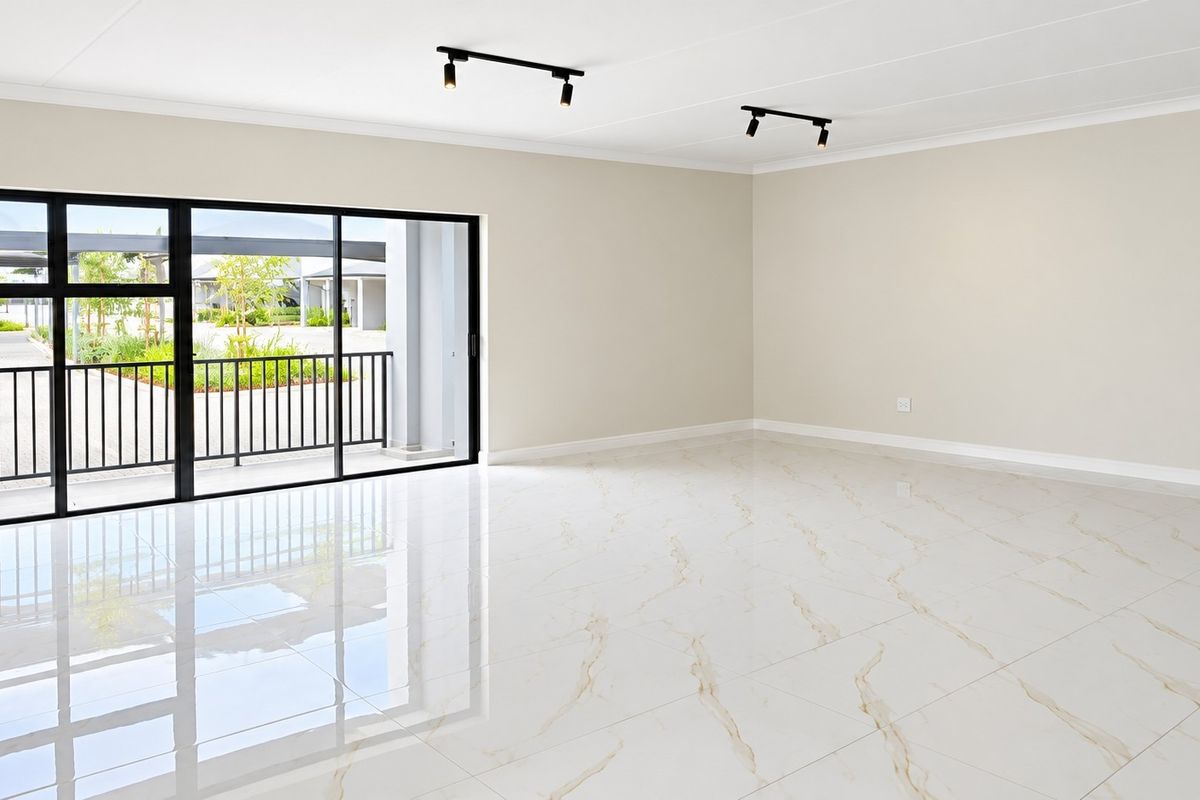 A bright, spacious, and empty living area featuring polished marble-look floor tiles, modern black track lighting, and large sliding doors opening to a balcony.
