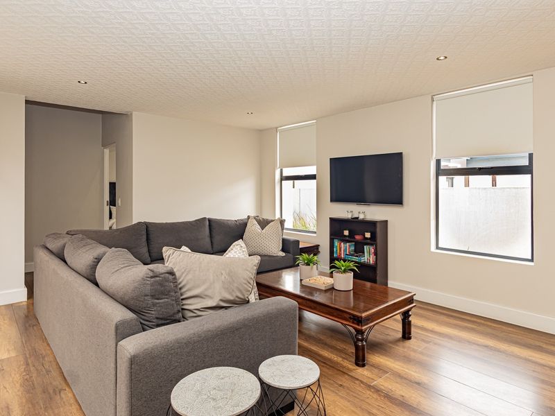 A well-lit living room featuring laminate flooring, recessed downlights, and a textured ceiling, providing a comfortable and functional space for relaxation.