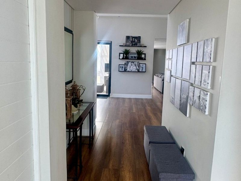 A bright and well-maintained hallway featuring wood-look tile flooring, recessed downlighting, and clean neutral wall finishes leading toward the living area.