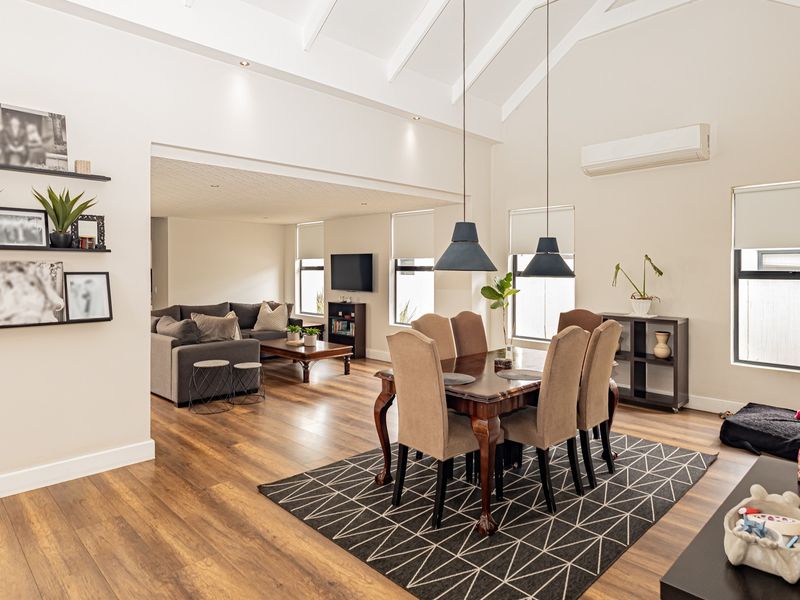 Spacious open-plan living and dining area featuring high vaulted ceilings, modern laminate flooring, recessed lighting, and a split-system air conditioner.