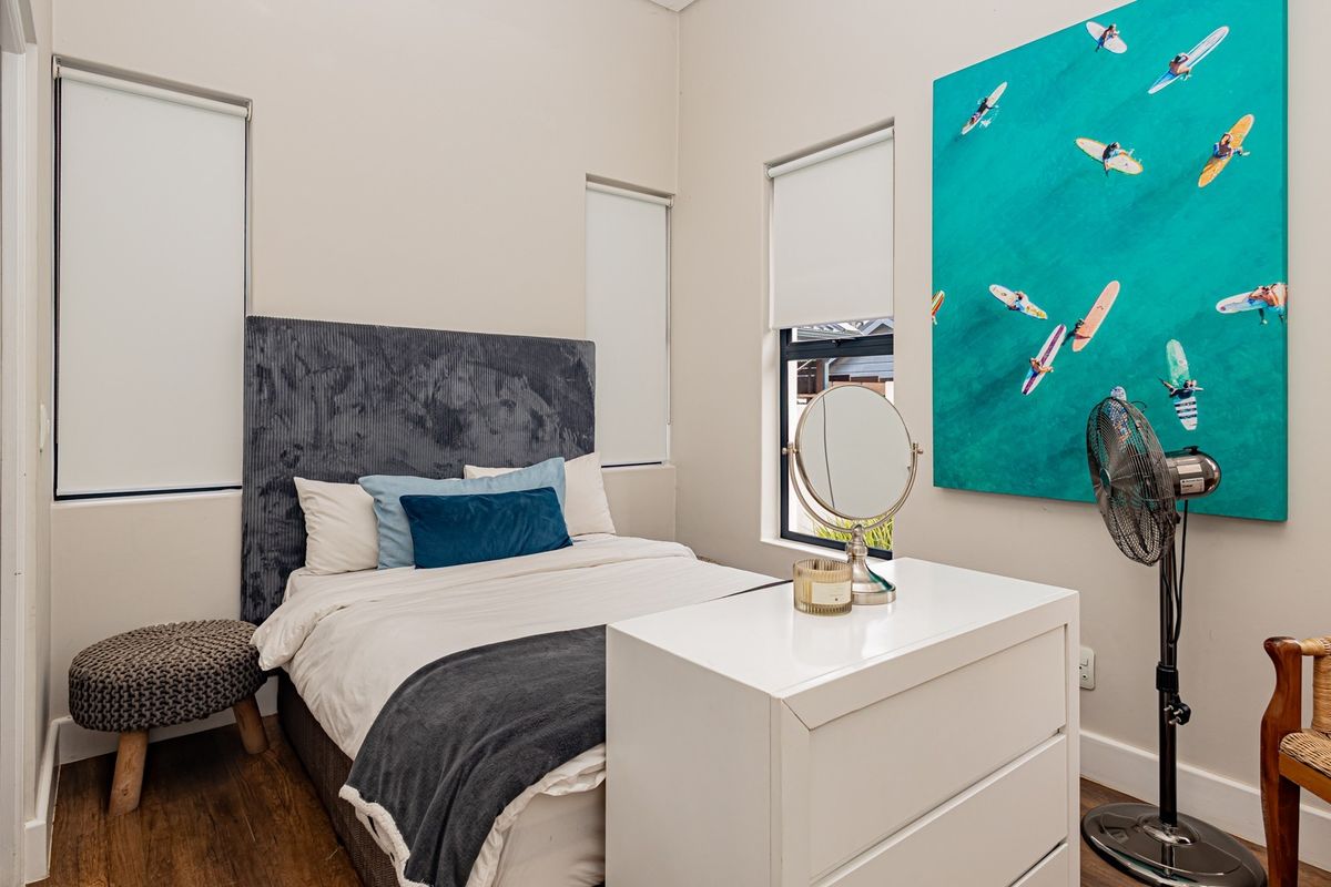 A well-maintained bedroom featuring laminate flooring, neutral walls, and modern aluminium window frames with fitted roller blinds.